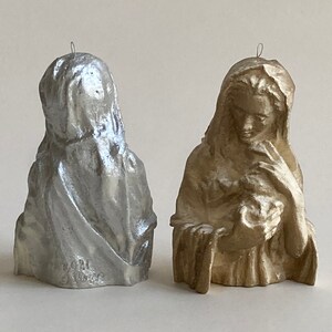 May include: Two small, decorative figurines of a woman holding a child. The figurine on the left is silver, and the figurine on the right is gold.
