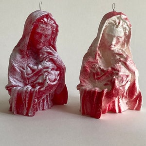 May include: Two red and white painted plaster figurines of the Virgin Mary holding a baby Jesus. The figurines are both wearing a robe and have a halo above their heads.