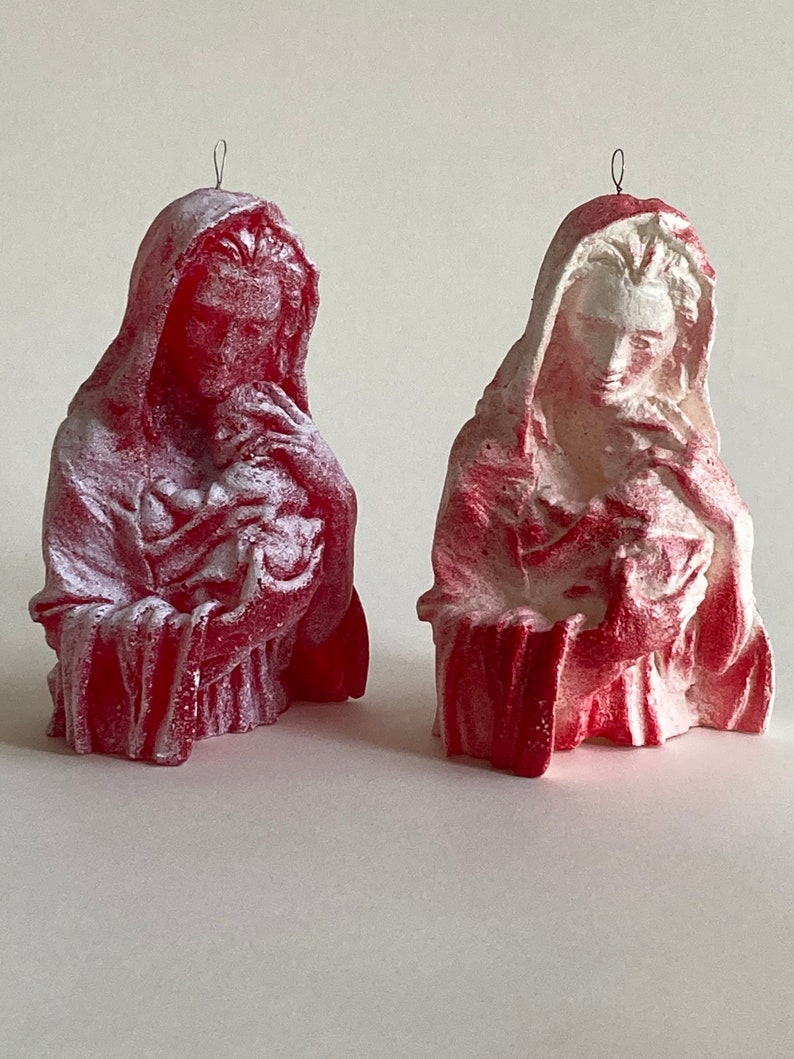 May include: Two red and white painted plaster figurines of the Virgin Mary holding a baby Jesus. The figurines are both wearing a robe and have a halo above their heads.