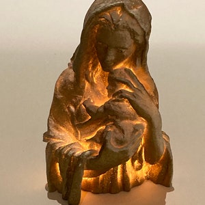 May include: A gold-toned figurine of the Virgin Mary holding a baby Jesus. The figurine is illuminated from within, creating a warm glow.