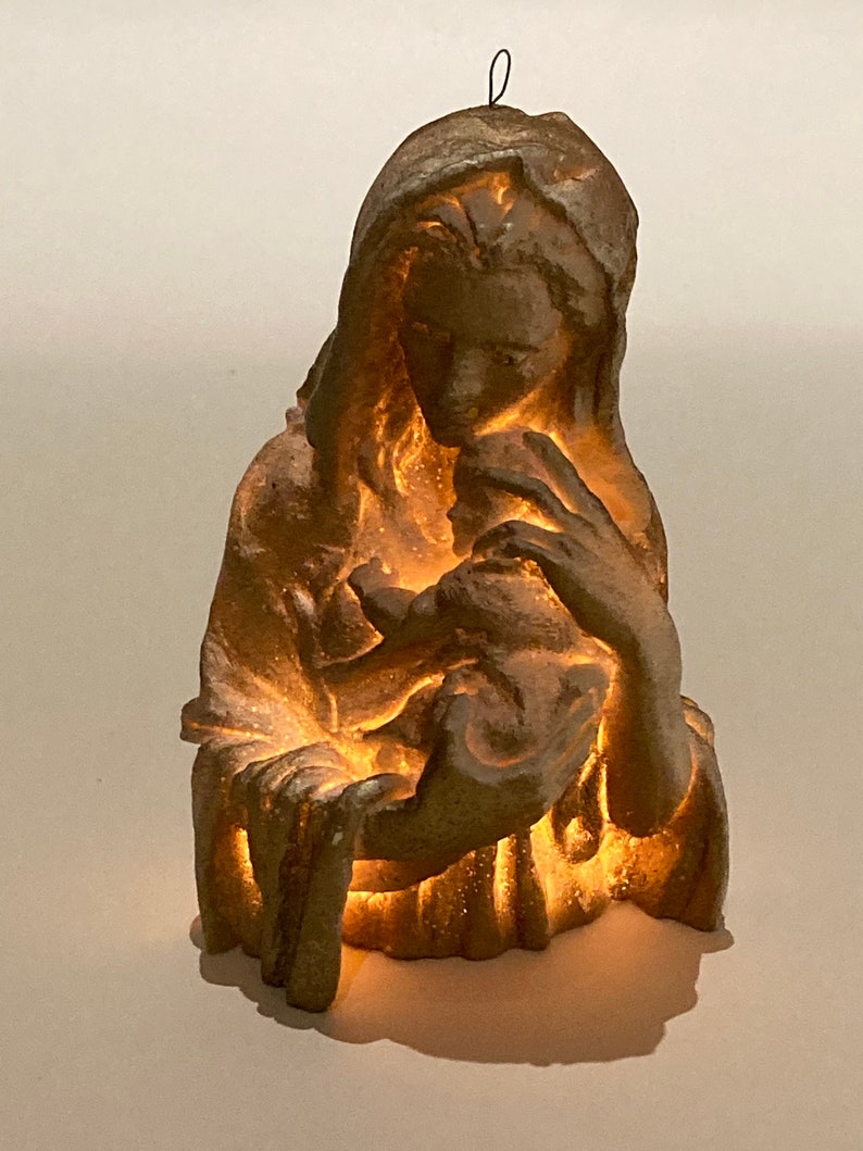 May include: A gold-toned figurine of the Virgin Mary holding a baby Jesus. The figurine is illuminated from within, creating a warm glow.
