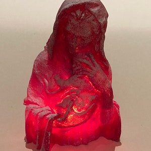 May include: A red, frosted, ceramic figurine of a woman holding a baby. The figurine is lit from within, creating a warm glow.