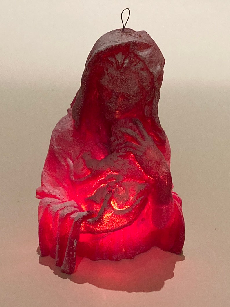 May include: A red, frosted, ceramic figurine of a woman holding a baby. The figurine is lit from within, creating a warm glow.