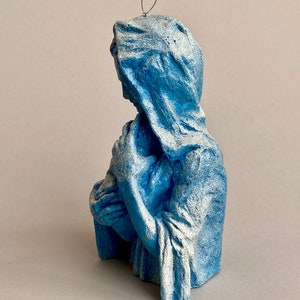 May include: A blue ceramic figurine of the Virgin Mary holding a baby Jesus. The figurine is painted in a light blue color with white accents.