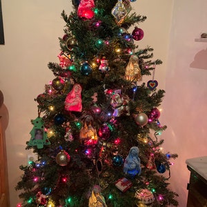 May include: A decorated Christmas tree with colorful lights and ornaments, including a blue, red, and gold figurine of the Virgin Mary, a wooden ornament with a child's photo and the name "Chiara", and a heart-shaped ornament.