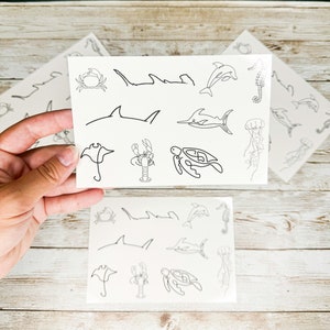 May include: Two sheets of temporary tattoos with a variety of sea creatures, including a crab, a seahorse, a dolphin, a stingray, a lobster, a turtle, and a jellyfish.