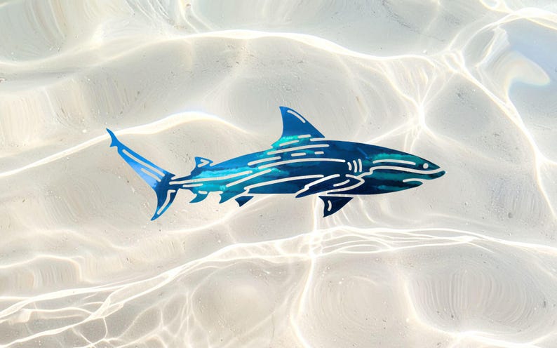 Puede incluir: Una pieza de arte mural de metal con forma de tibur&oacute;n, que presenta un acabado azul profundo con recortes lineales en azul claro y blanco que crean una sensaci&oacute;n de movimiento y textura en el cuerpo, las aletas y la cola del animal.