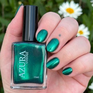 May include: A rectangular glass bottle of Azura Colour nail polish with a black cap, containing 15ml of metallic emerald green liquid. The label features the text Azura colour and 15ml. The fingernails are painted in the same metallic green.