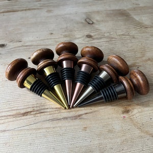 May include: Seven wooden wine bottle stoppers with different coloured metal tops. The stoppers are arranged in a semi-circle on a wooden surface.