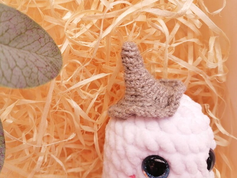 May include: A pink crocheted stuffed animal with a brown crocheted hat. The animal has large black eyes and a small pink nose.