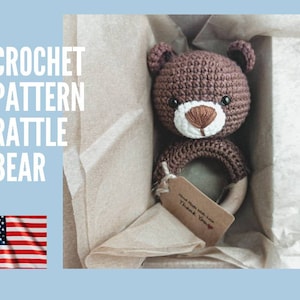 Peut inclure: Un hochet ours au crochet marron avec un anneau en bois, présenté dans une boîte. L'image affiche le texte "CROCHET PATTERN RATTLE BEAR". Une petite étiquette indique "Hand Made With Love Thank You".