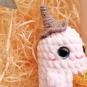 May include: White crocheted ghost holding a small orange crocheted pumpkin. The ghost has a gray crocheted hat and blue sparkly eyes.