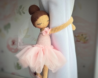 Peut inclure: Une poupée ballerine au crochet servant d'embrasse de rideau, avec une coiffure en chignon marron, un corsage rose pâle et un tutu en tulle superposé. La poupée a des yeux brodés fermés et porte des chaussons de danse rose pâle autour d'un rideau blanc.