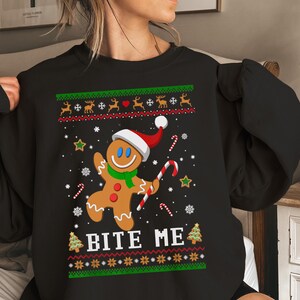 May include: Black Christmas sweater with a gingerbread man wearing a Santa hat and the text "Bite Me". The sweater has a green and red holiday pattern.