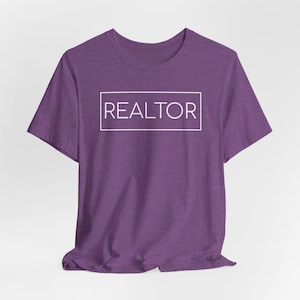 May include: A purple t-shirt with the word "REALTOR" in a white rectangular box. The shirt has short sleeves and a crew neck. The fabric has a heathered texture.