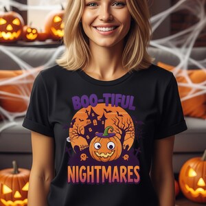May include: Black t-shirt with a Halloween-themed graphic. The design features a smiling jack-o'-lantern wearing a witch's hat, a haunted house, and the words "BOO-TIFUL NIGHTMARES" in purple and orange. Pumpkins are in the background.