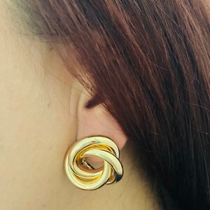 May include: Gold-toned knot-shaped earrings. The earrings are made of three interlocking circles.