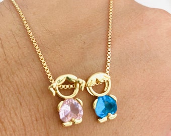 May include: A gold chain necklace with a pendant featuring two figures, one with a pink gemstone and the other with a blue gemstone.