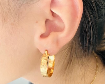 May include: Gold hoop earrings with a textured design. The earrings are worn in a person's ear.