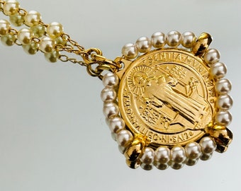 May include: A gold necklace with a St. Christopher medal pendant surrounded by a circle of white pearls. The medal features a depiction of St. Christopher carrying a child.
