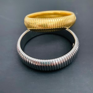 May include: Two metal bracelets, one silver and one gold, with a ribbed texture. The bracelets are stacked on top of each other.