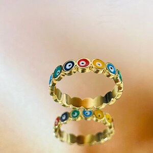 以下が含まれることがあります： カラフルな邪眼チャームのバンドが付いた金のリング。チャームはバンドの周りに円形に配置され、すべて同じ方向を向いています。このリングは、保護と幸運の象徴として人気があります。