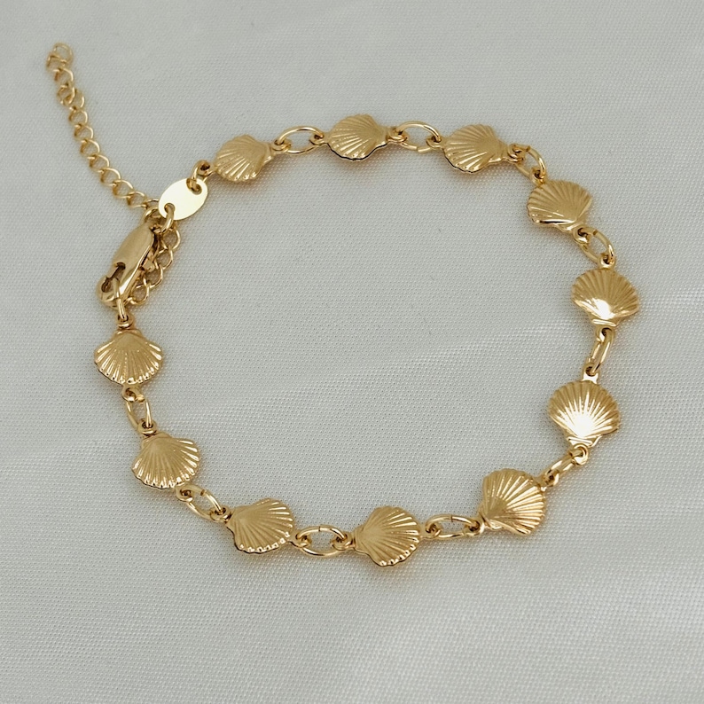 May include: A gold chain bracelet with a series of small seashell charms. The bracelet has a lobster clasp closure.