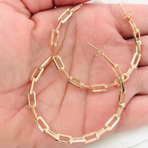 May include: Gold hoop earrings with a chain link design. The earrings are large and have a simple, modern style.