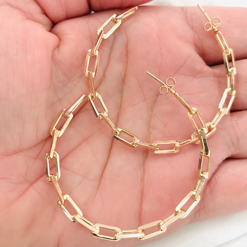 May include: Gold hoop earrings with a chain link design. The earrings are large and have a simple, modern style.