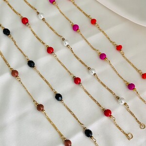 May include: A set of six gold chain necklaces with different colored beads, including red, black, white, pink, and orange. The necklaces are displayed on a white surface.