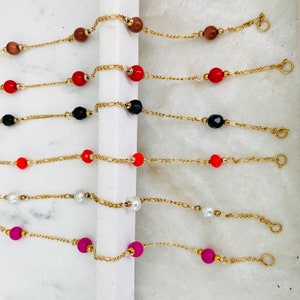 May include: Seven gold chain bracelets with different colored beads. The beads are red, black, white, orange, and pink.