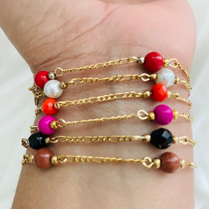 May include: A set of seven gold chain bracelets with colorful beads. Each bracelet features a different colored bead, including red, white, orange, pink, black, and brown.
