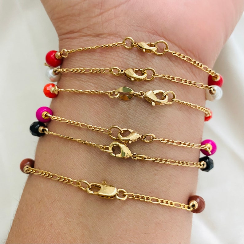 May include: A set of six gold chain bracelets with colorful beads. Each bracelet features a different color bead, including red, pink, black, brown, white, and orange.