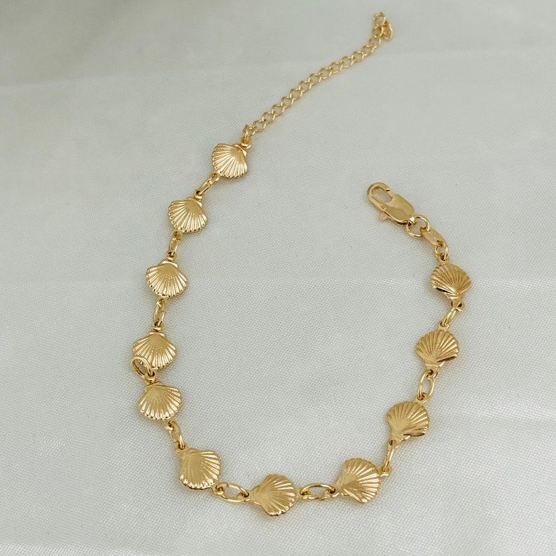 May include: A gold-toned bracelet featuring a delicate chain and a series of small seashell charms.