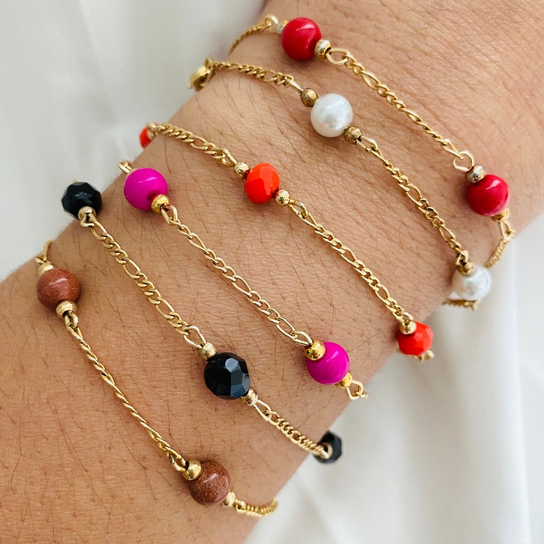 May include: A set of gold chain bracelets with colorful beads. The bracelets feature different colored beads, including red, orange, pink, black, and brown.