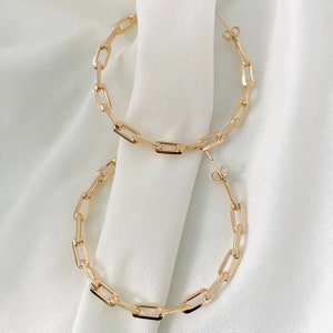 May include: A pair of gold hoop earrings with a chain link design. The earrings are large and have a simple, modern style.