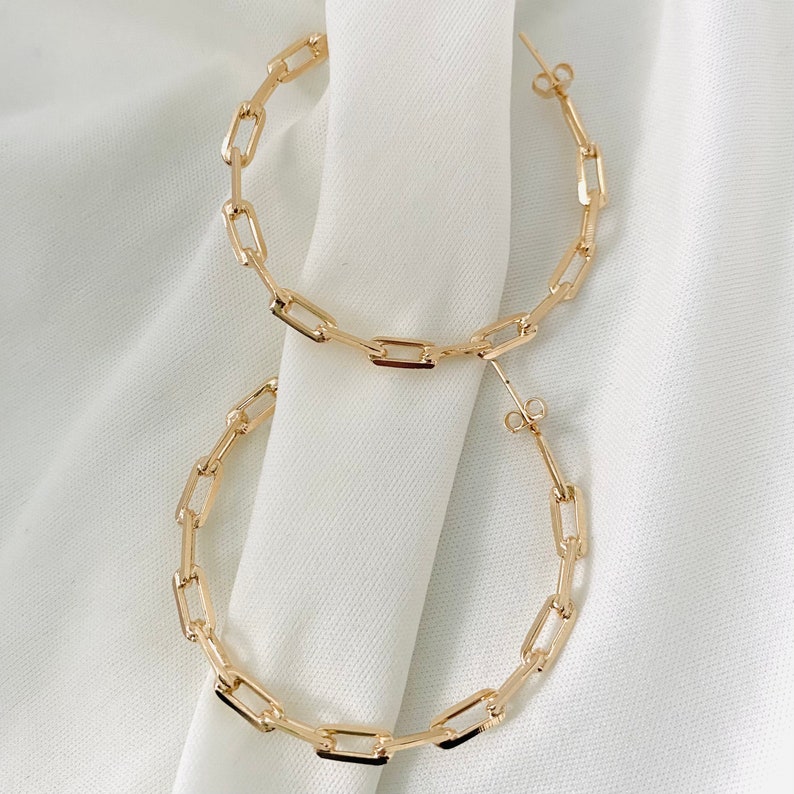 May include: A pair of gold hoop earrings with a chain link design. The earrings are large and have a simple, modern style.