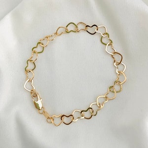 Puede incluir: Un brazalete de cadena de oro en forma de coraz&oacute;n. El brazalete est&aacute; hecho de eslabones entrelazados en forma de coraz&oacute;n.