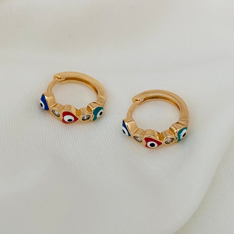 K&ouml;nnte beinhalten: Ein Paar goldene Creolen mit einem Design aus blauen, roten und wei&szlig;en b&ouml;sen Augen.