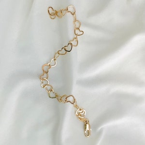 Puede incluir: Un brazalete de cadena dorada en forma de coraz&oacute;n con cierre de langosta.