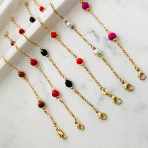 May include: Six gold chain bracelets with different colored beads. The beads are red, black, white, and pink.