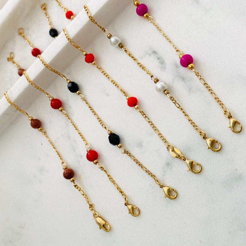 May include: Six gold chain bracelets with different colored beads. The beads are red, black, white, and pink.