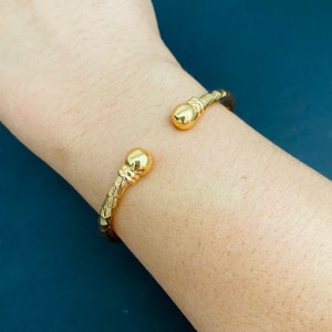 May include: A gold bangle bracelet with a textured design and round ball accents at each end.
