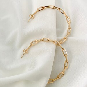 May include: A pair of gold hoop earrings with a chain link design. The earrings are large and have a simple, modern style.
