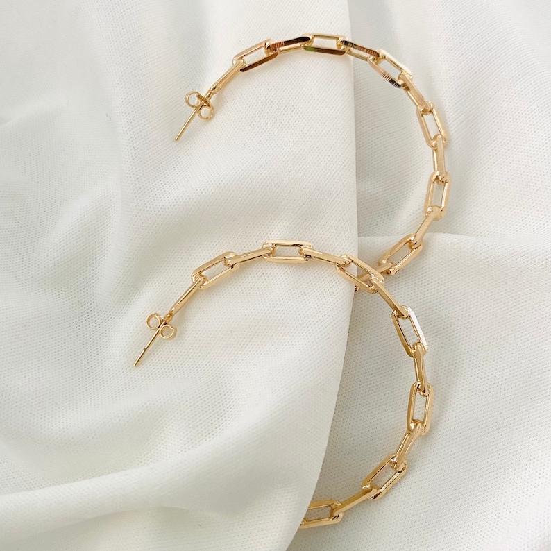 May include: A pair of gold hoop earrings with a chain link design. The earrings are large and have a simple, modern style.