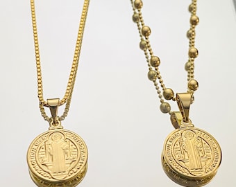 May include: Two gold necklaces with pendants. One necklace has a delicate chain and a round pendant with a religious image. The other necklace has a thicker chain with round beads and a similar pendant.