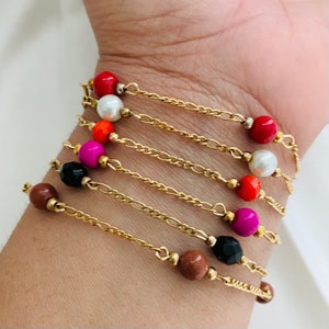 May include: A set of seven gold chain bracelets with colorful beads. The beads are red, white, pink, black, and brown.