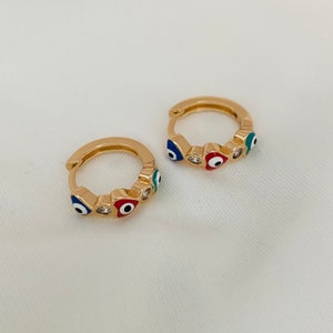K&ouml;nnte beinhalten: Ein Paar goldene Creolen mit einem Design aus blauen, roten und gr&uuml;nen b&ouml;sen Augen. Die Ohrringe sind klein und zart.