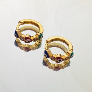 K&ouml;nnte beinhalten: Goldene Creolen mit einem Design aus mehreren blauen, roten und gr&uuml;nen b&ouml;sen Augen. Die Augen sind von kleinen klaren Strasssteinen umgeben.