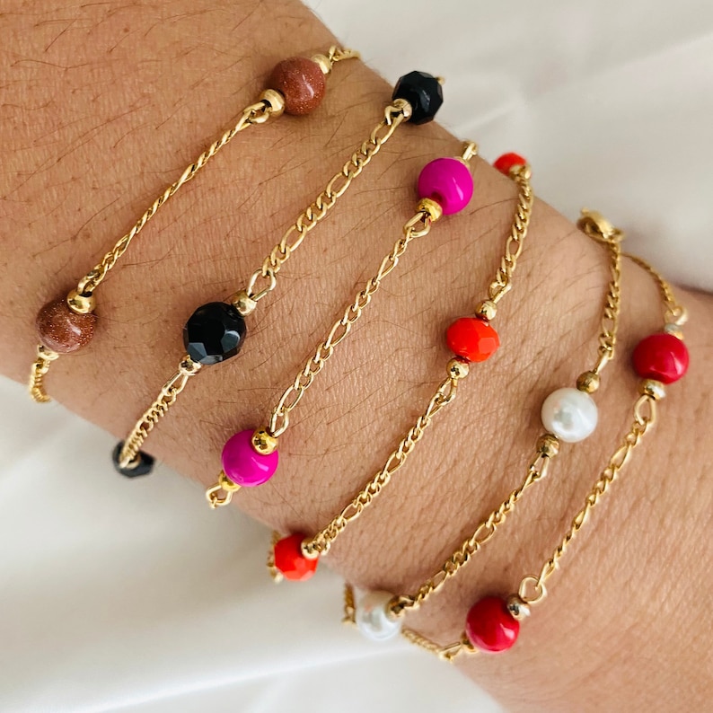 May include: Five gold chain bracelets with colorful beads. The bracelets feature red, orange, pink, black, and brown beads.